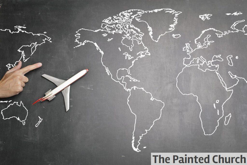 Top view of miniature airplane placed on over gray world map with crop hand of anonymous person indicating direction representing travel concept
