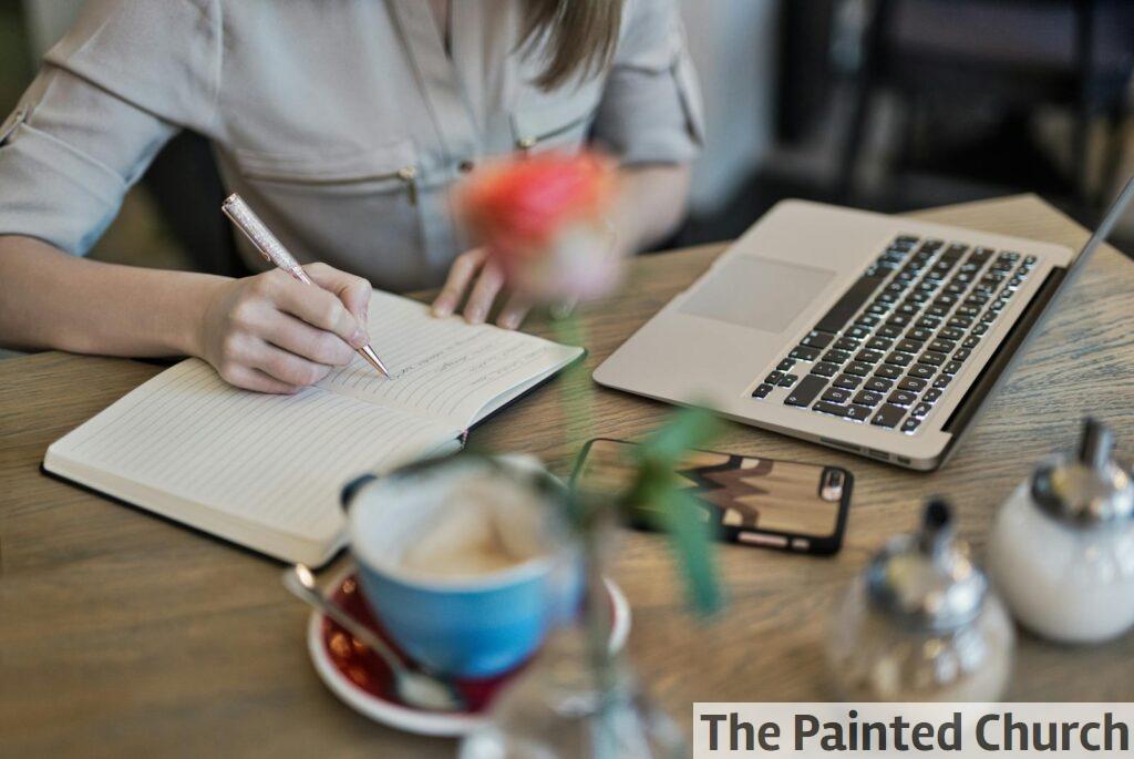 Person Writing On A Notebook Beside Macbook