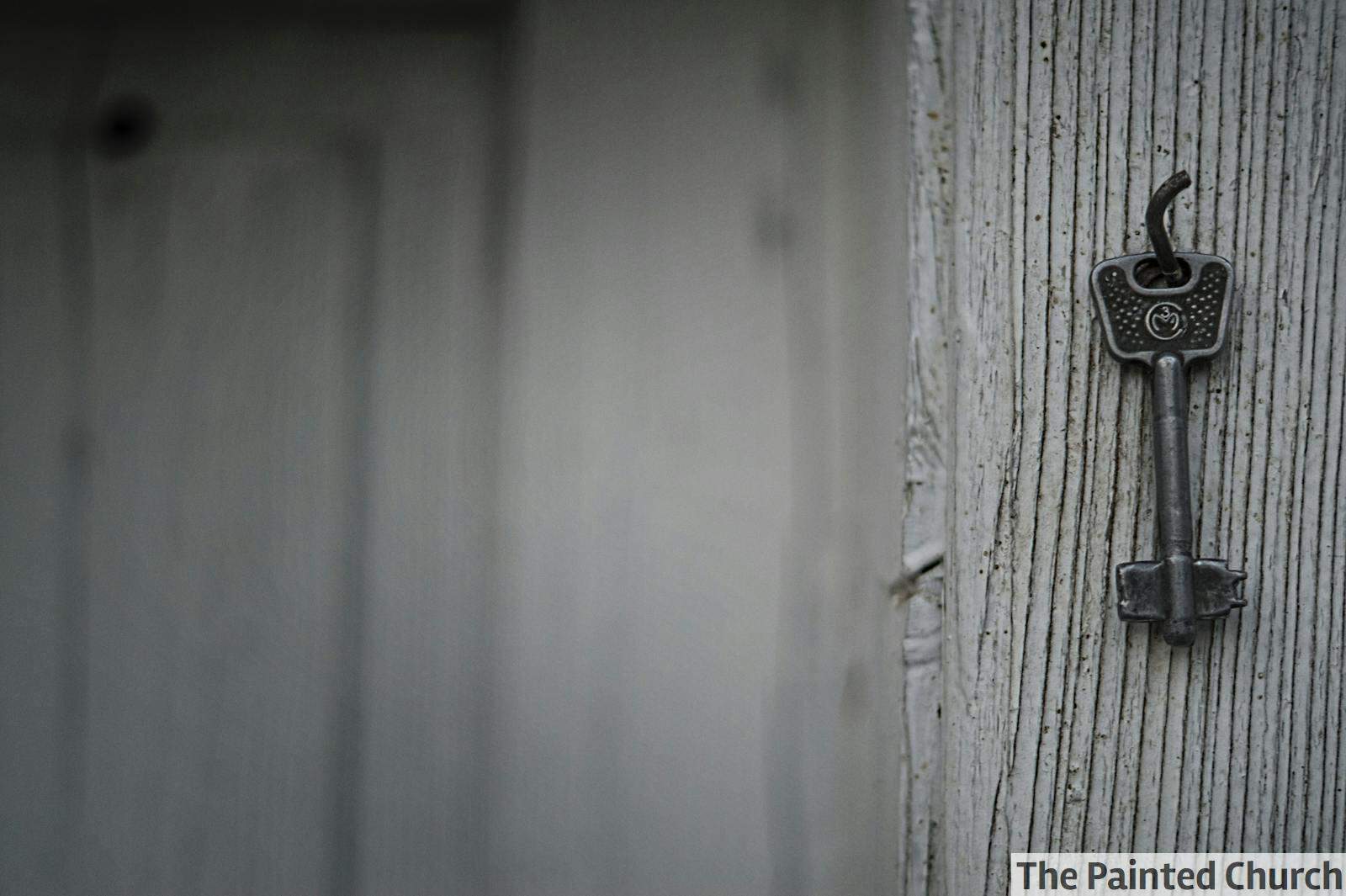 A vintage iron key hangs on a textured weathered wooden wall, evoking nostalgia and mystery.