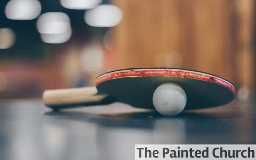 Close-up of a ping pong paddle and ball on a table with an artistic bokeh background, indoors.