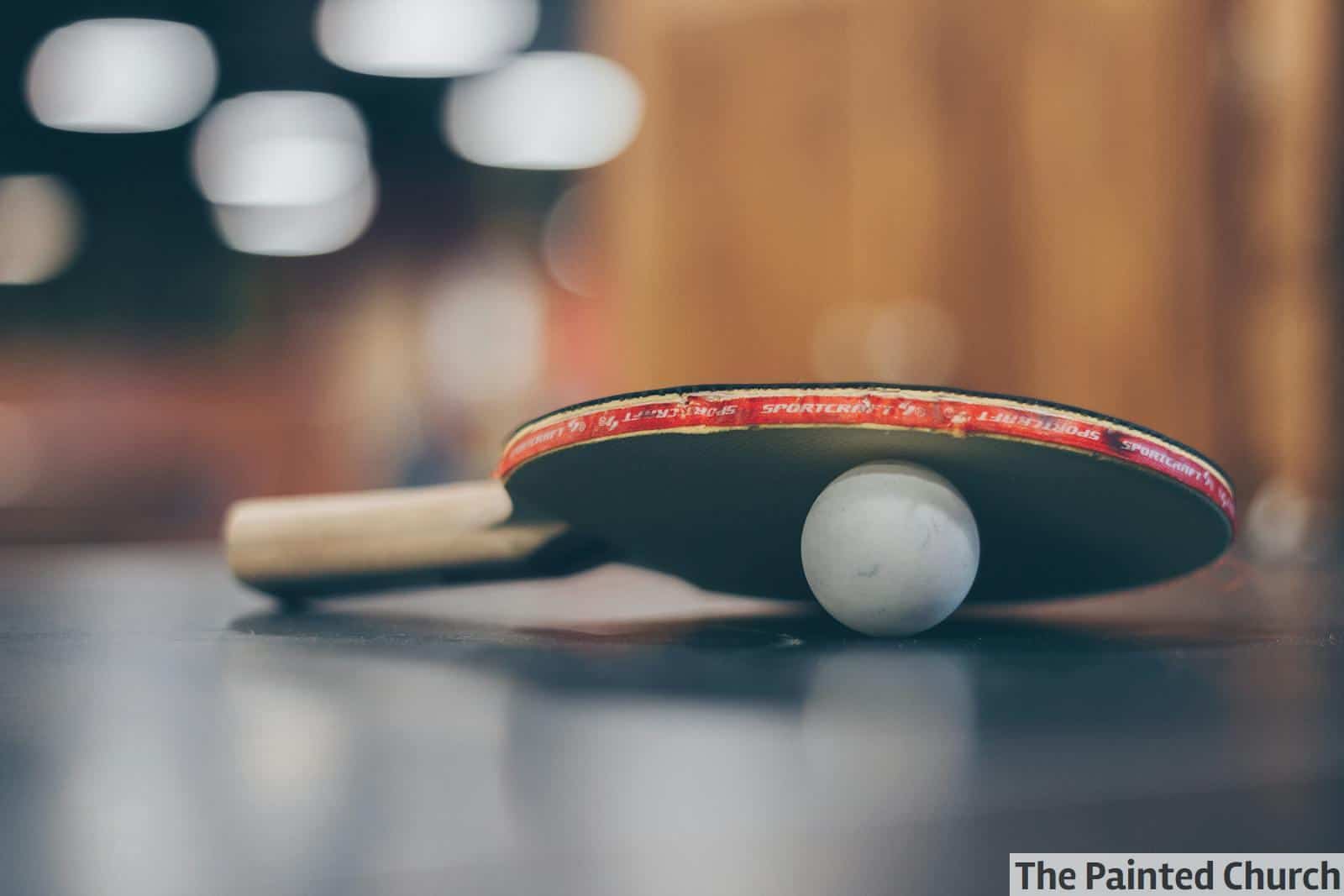 Close-up of a ping pong paddle and ball on a table with an artistic bokeh background, indoors.